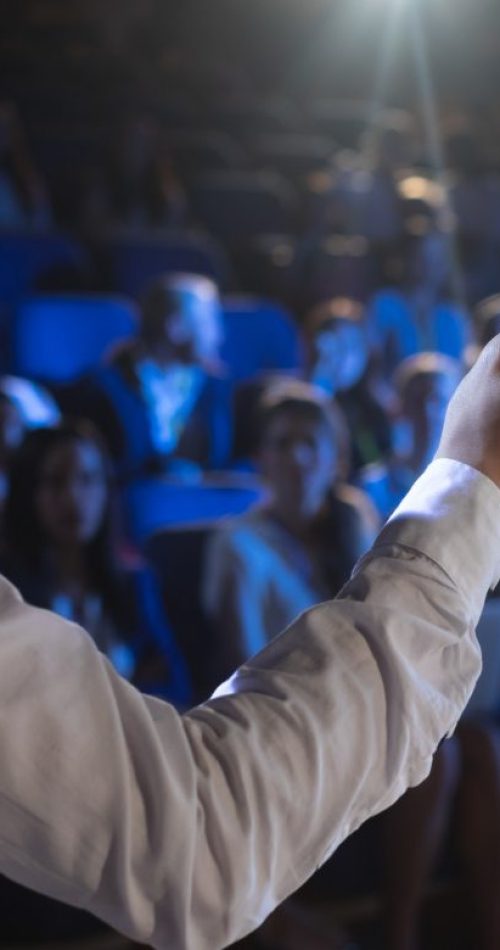 rear-view-of-caucasian-businessman-giving-presentation-in-front-of-audience-in-auditorium.jpg